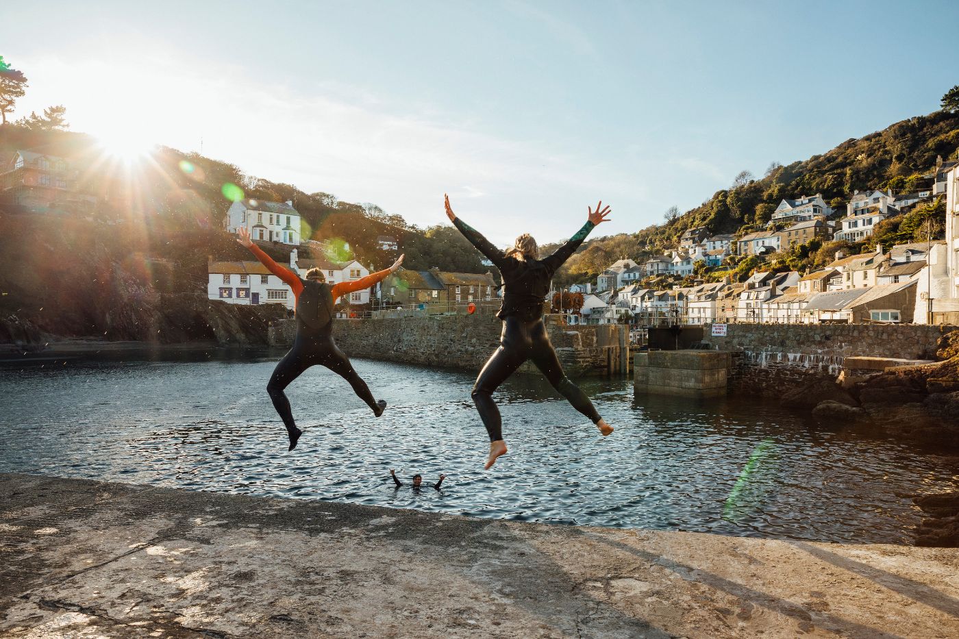 Two people in wetsuits jumping off harbour together in Cornwall